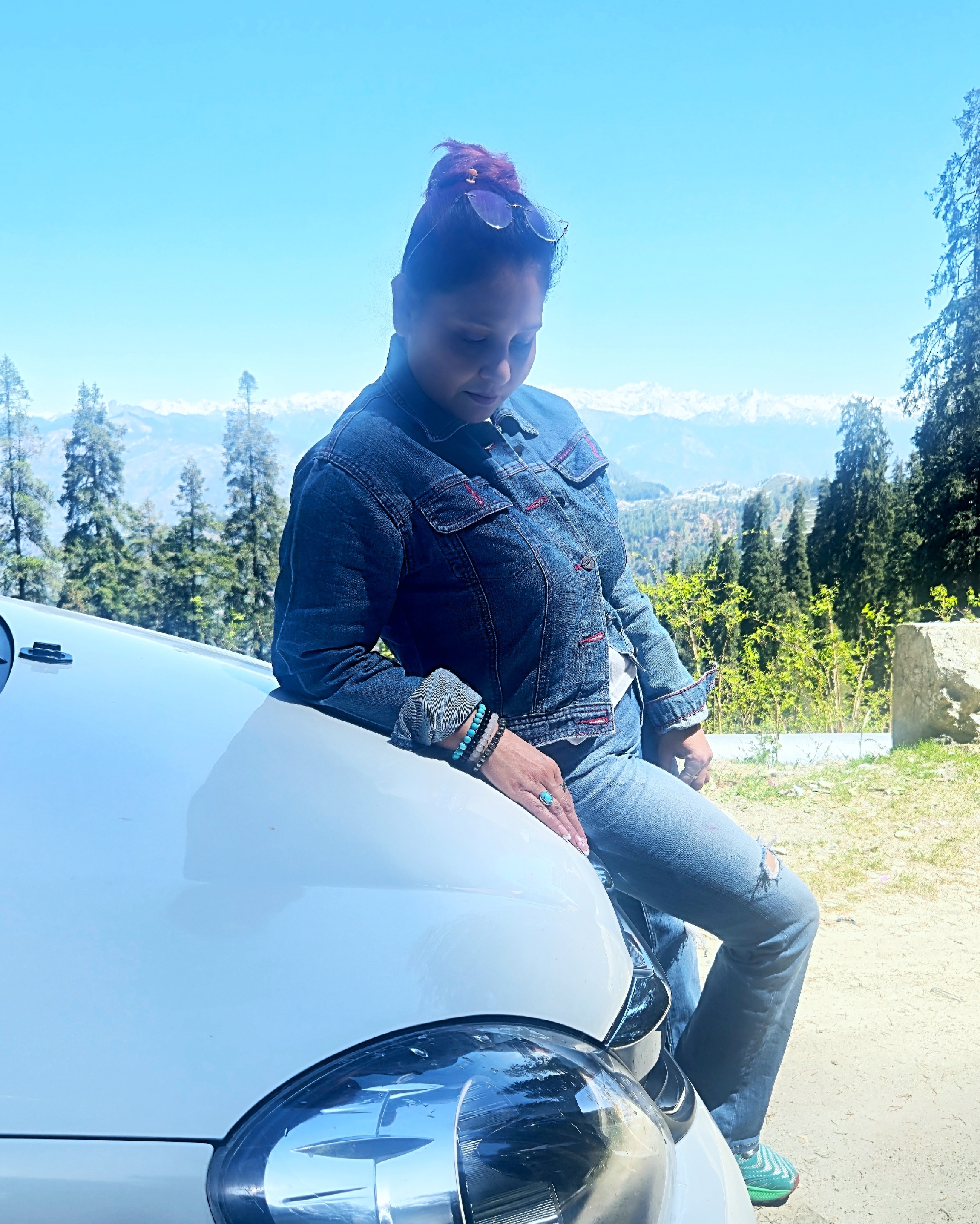 Person resting against a car in the mountains with serene landscape in the background.